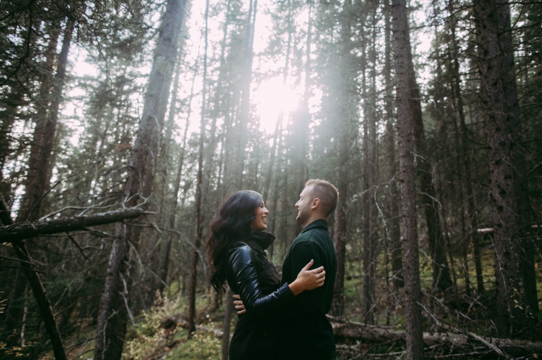 beautiful couple smile at each other in the forest in Banff, Alberta