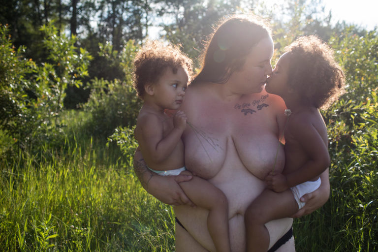 topless mom holds both her daughers for outdoor portrait