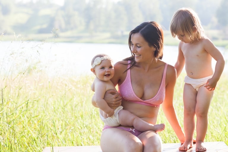 mom and her two daughters sit near lake for portrait