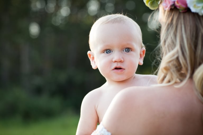 blue eyed toddler peeks over his mom's shoulder