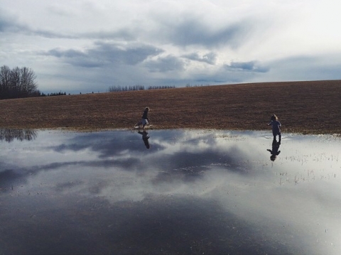 farm kids play in a huge puddle during Alberta spring near Edmonton, Alberta, Canada