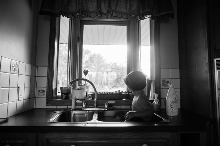 a kid takes a bath in the farmhouse sink creating a beautiful black and white environmental portrait