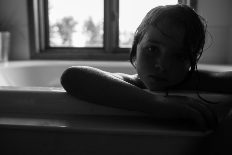 little girl leans over the side of the bathtub during family photography session