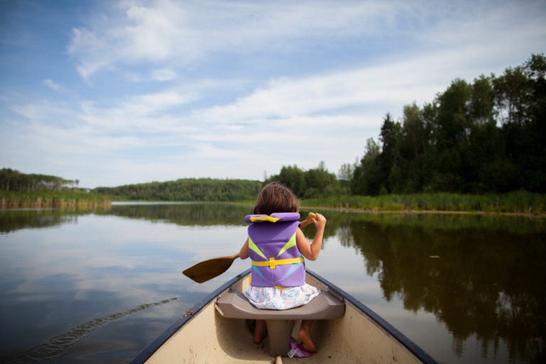 child paddles in the front seat of the canoe on a small Albert lake