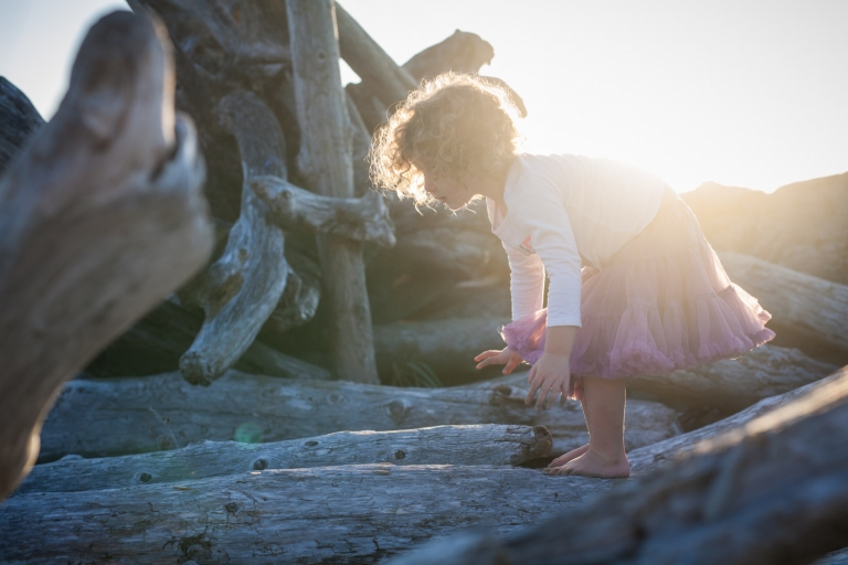 curly-haired toddler climbing on driftwood during documentary family session