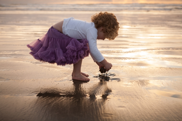 little girl plays on Tofino beach at sunset for a candid photograph by Edmonton family photographer Jenna Hobbs