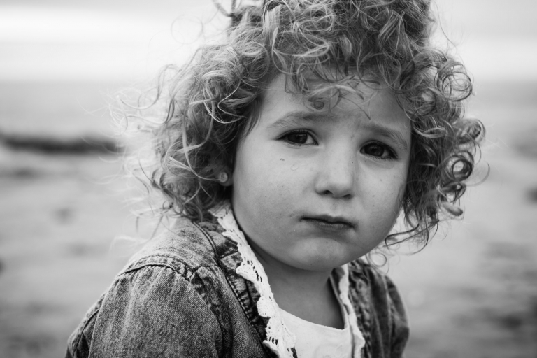 honest black and white portrait of little girl looking at camera on beach