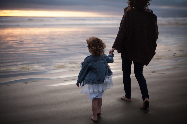 mother and child hold hands walking on beach at sunset for candid family photography