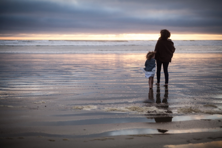 mother and daughter stand on Tofino beach at sunset