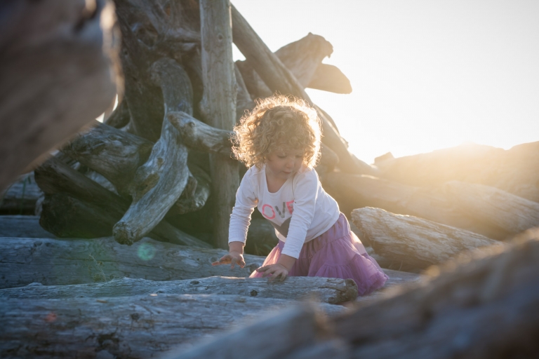 natural light portrait outdoors of curly-haired girl with driftwood