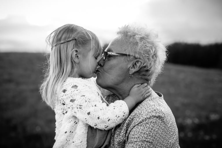 child kisses her great grandmother in an emotive black and white portrait by Edmonton's best family photographer