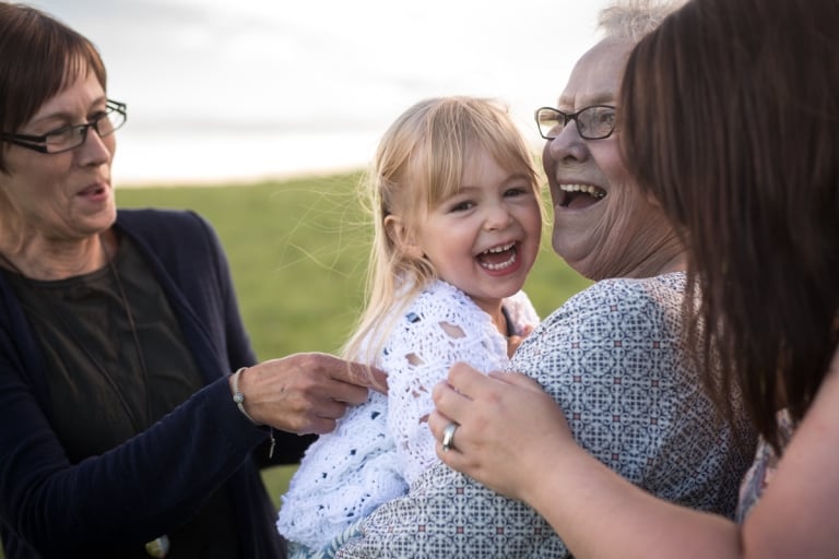 granddaughter giggles while grandma and mom tickle her