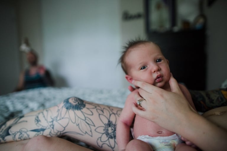 newborn baby looks directly at camera as he's burped during a lifestyle newborn photo session by Edmonton family photographer Jenna Hobbs