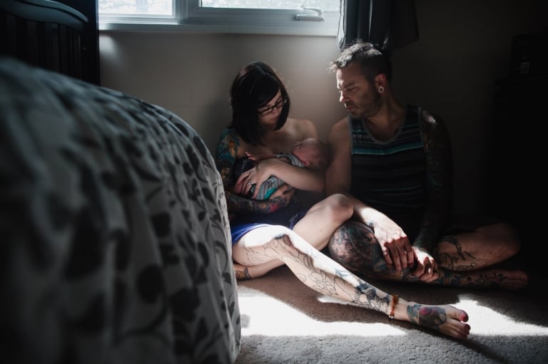 tattooed mom and dad sit in their bedroom with their newborn baby boy