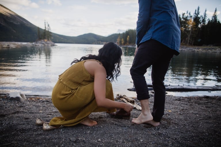 couple take off their shoes to walk into mountain lake