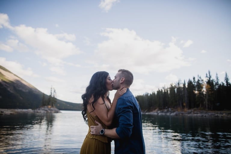couple kiss at Lake Minnwanka during engagement session by Edmonton wedding photographer Hobbs Photography