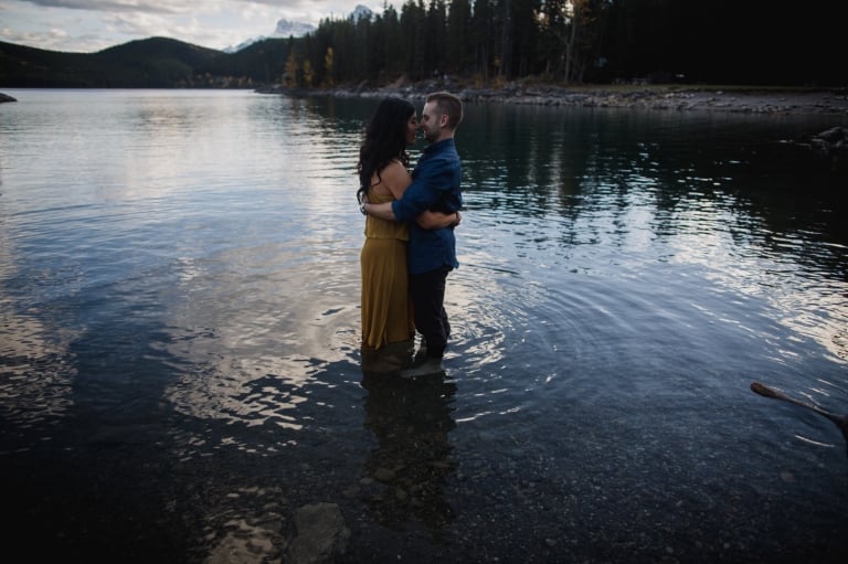 engaged couple cuddle in mountain lake in Banff