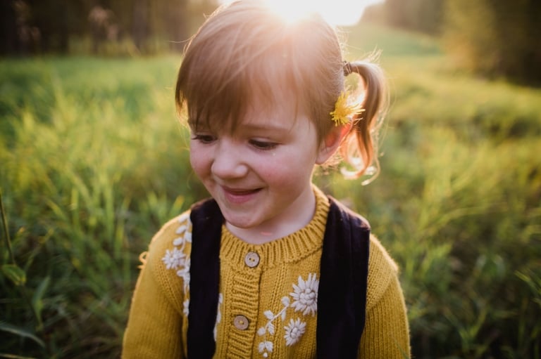 child in field with dandelion behind her ear
