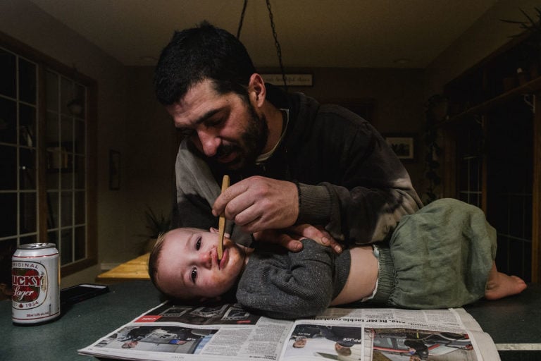 dad brushes toddler's teeth while laying on counter