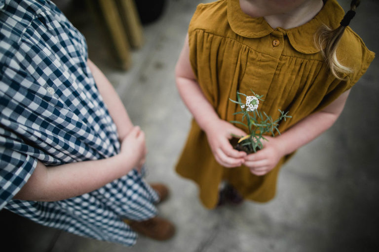 child in mustard dress holds small plant
