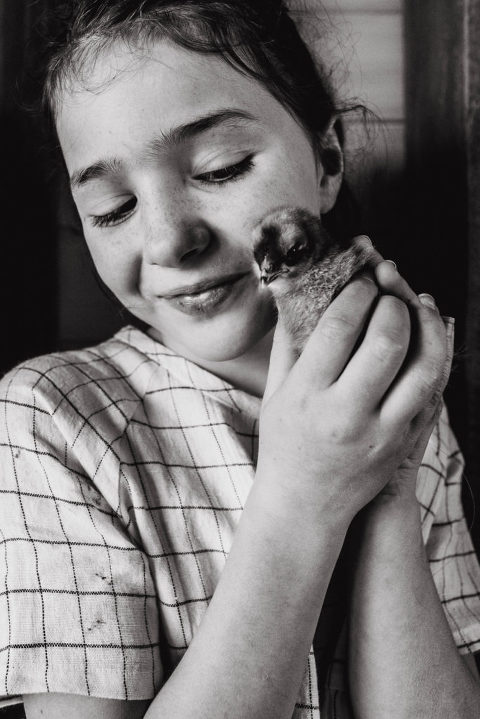 a girl holds a baby chick to her cheek