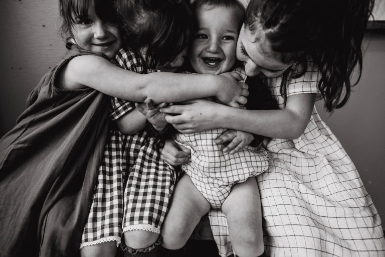 three big sisters hug their baby brother during photoshooot for CLOTH