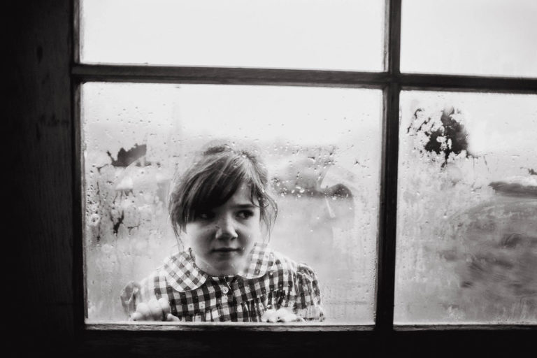 girl in plaid dress presses her face to the window