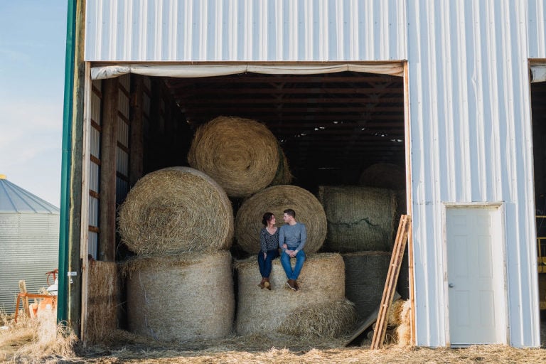 couple sits on a round bale and talk
