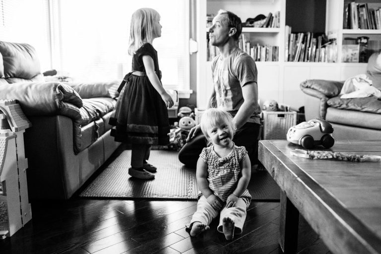 toddler with Down's syndrome gives a cheeky grin in front of her dad and older sister