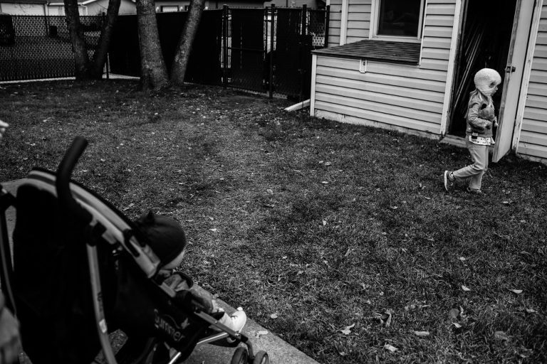 little sister sits in the stroller as big sister walks across the lawn