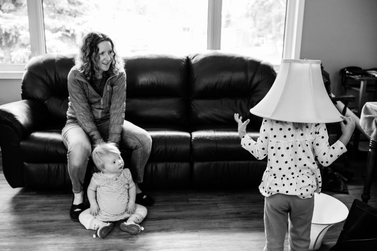 little girl puts lamp shade on her head as her mom and sister watch