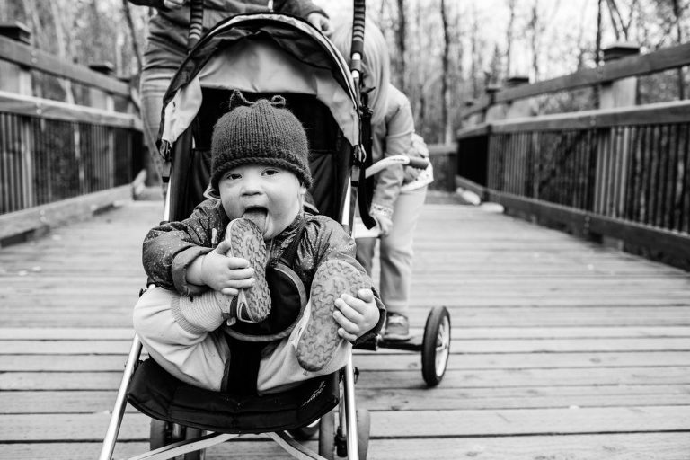 toddler licks her shoes while sitting in stroller on family walk