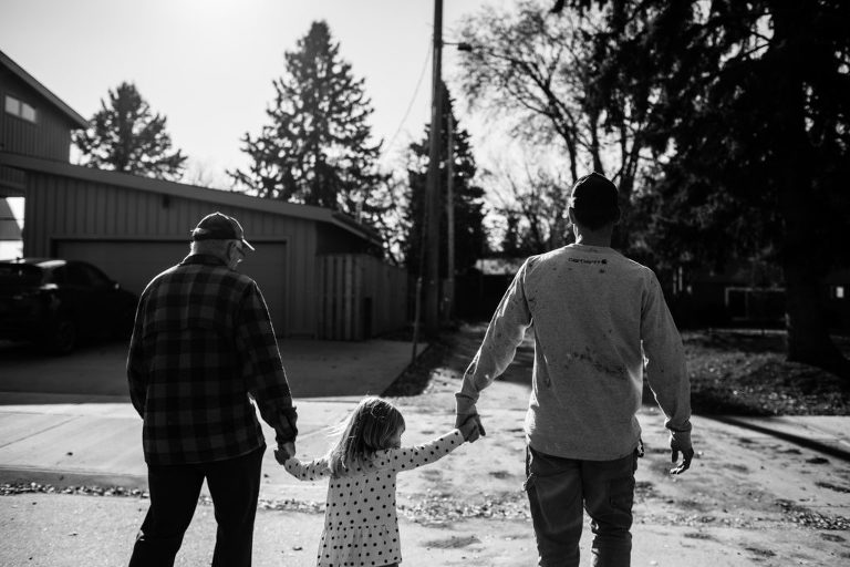 little girl holds hands with her dad and grandpa as they walk in Edmonton