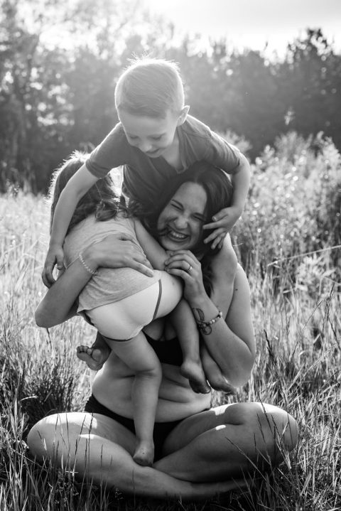 black and white portrait of Edmonton yoga teacher Devon Andersen and her two children climbing on her outside near Edmonton