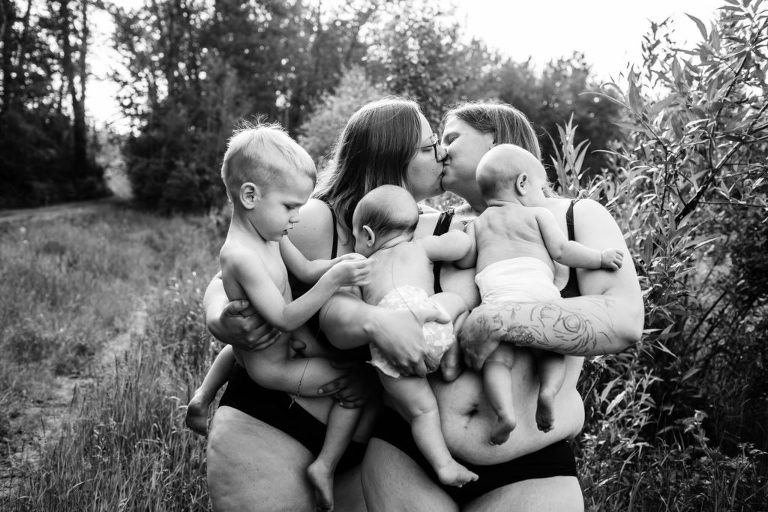 black and white portraits of two moms kissing while they hold their three children