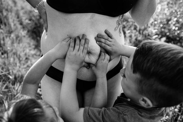 black and white detail photo of children squeezing their mom's stomach