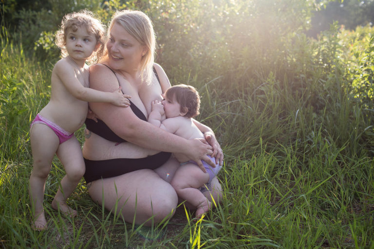 little girl hugs her mom as she breastfeeds her infant daughter