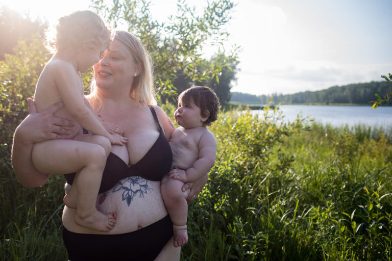 plus size mom holds both her daughers in photo session celebrating self love and postpartum beauty